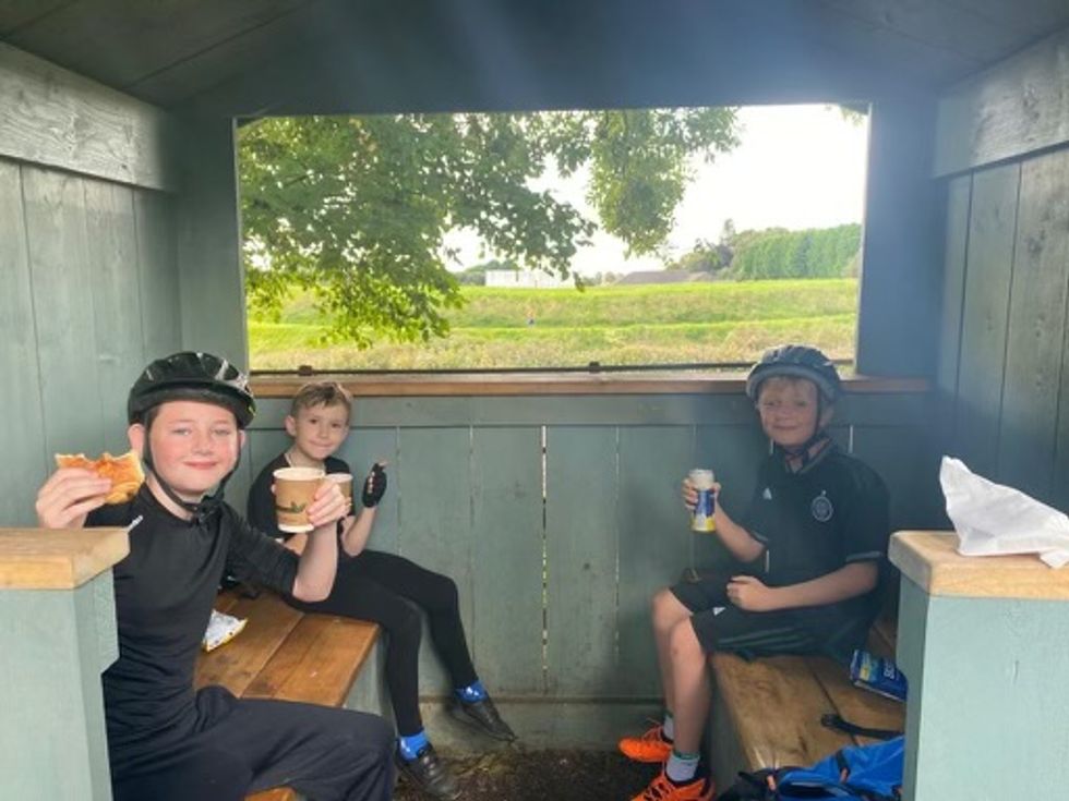 Three of the boys sat on a bench wearing bike helmets