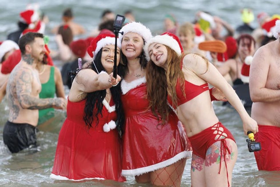 Three women pose for a selfie in the sea during annual Santa Splash