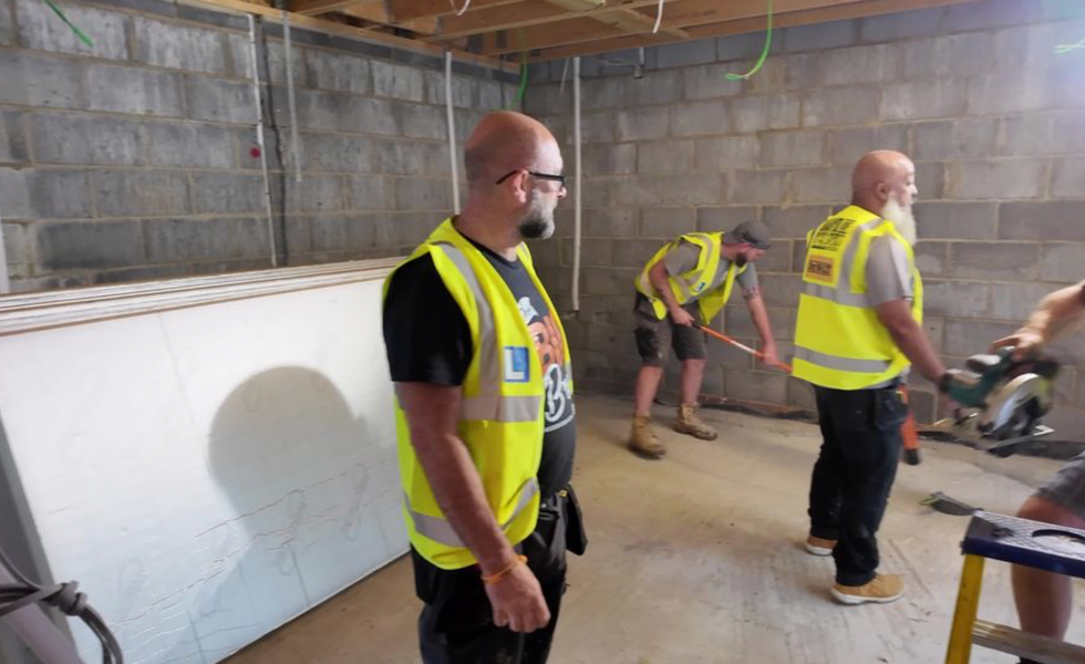 Three workmen in a room, which has breezeblock walls and timber panels on the ceiling