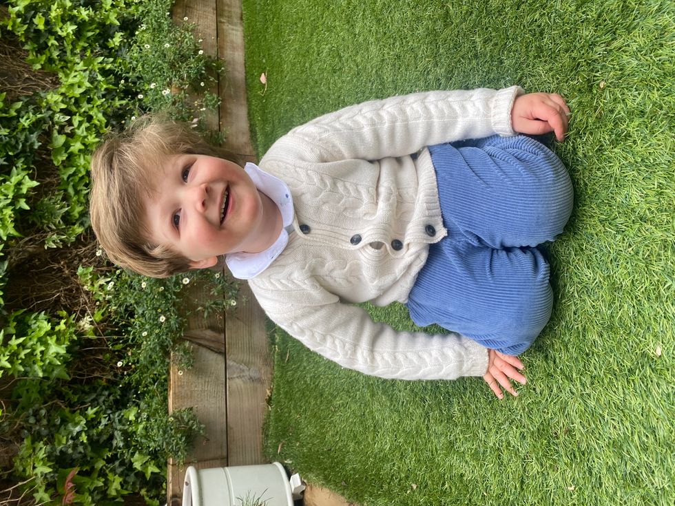 Three-year-old Nathaniel Clayton kneeling down on the grass smiling