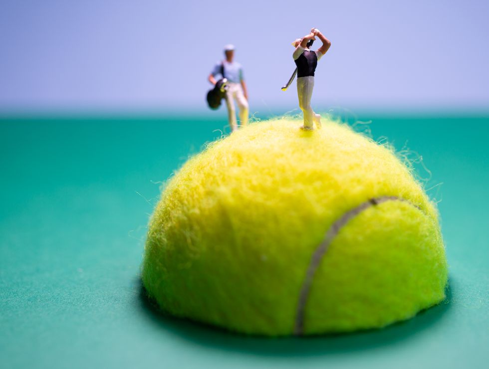 Tiny figures posed playing golf, on the top of a tennis ball which has been cut in half