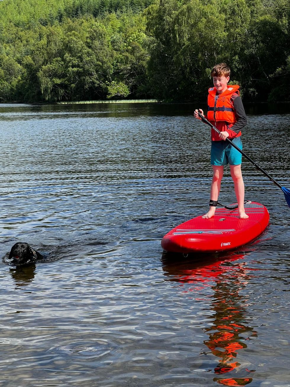 Toby Peart smiling while paddleboard, with a dog swimming in the water next to him