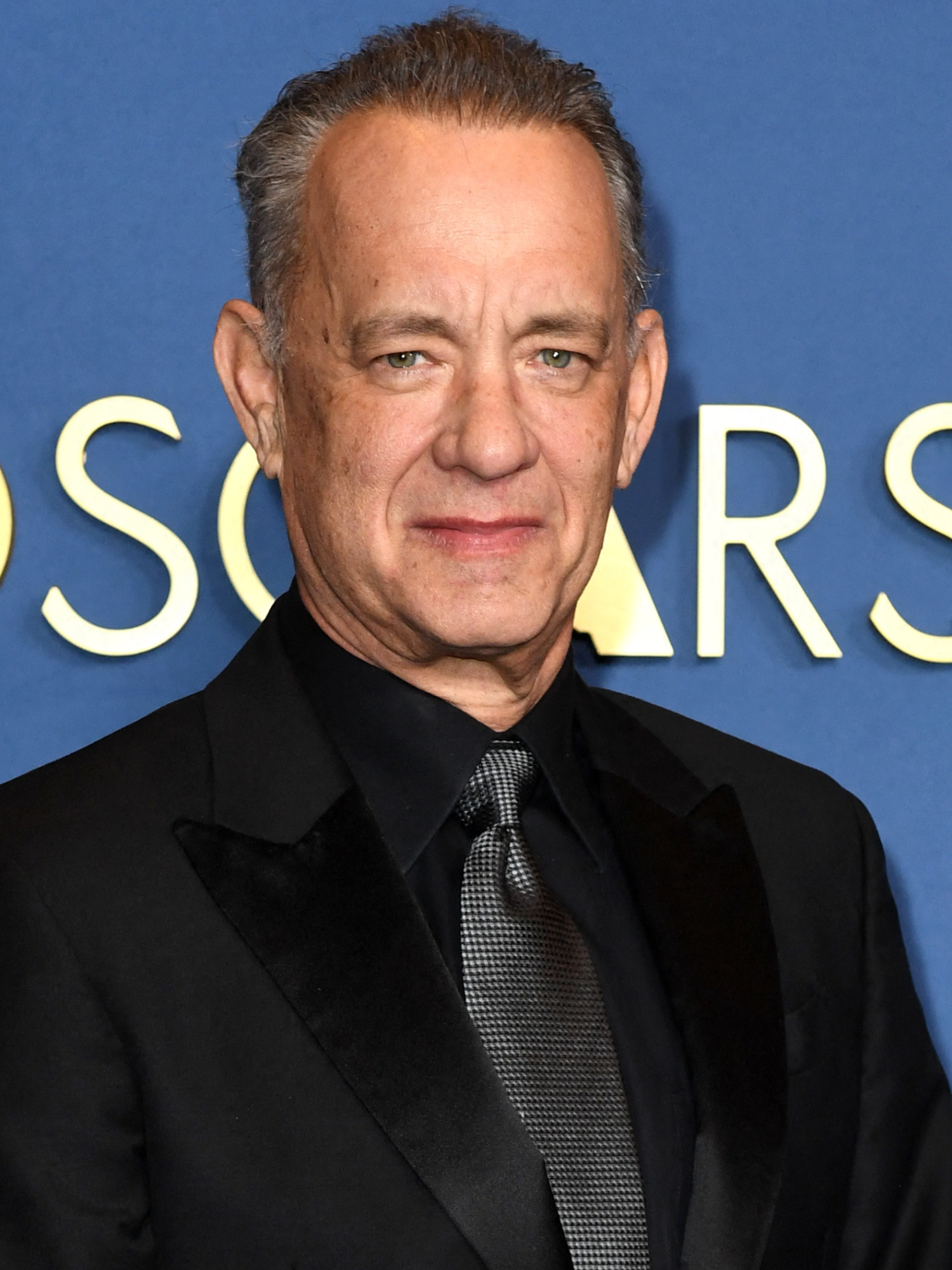 Tom Hanks in front of a blue Oscars postarboard.