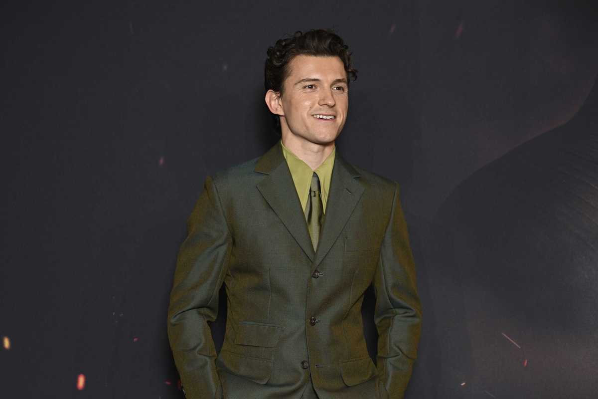 Tom Holland, a young white man with curly brown hair, in a green suit at a red carpet event for The Odyssey.