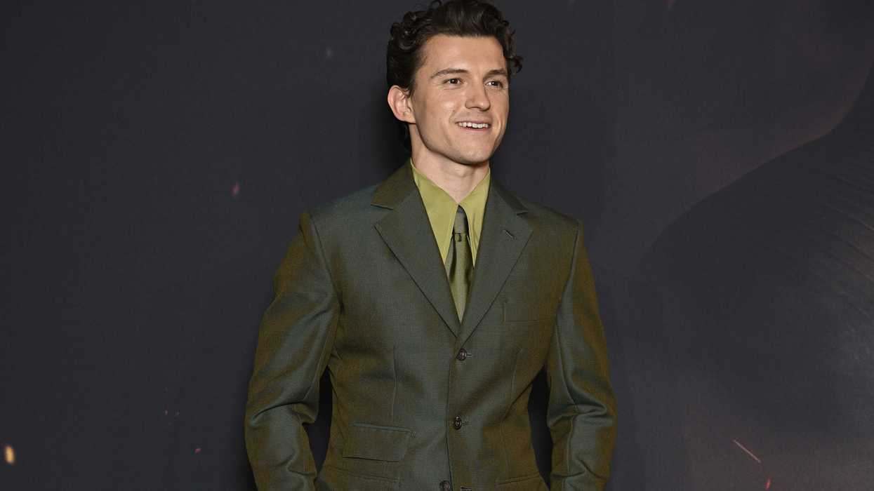 Tom Holland, a young white man with curly brown hair, in a green suit at a red carpet event for The Odyssey.