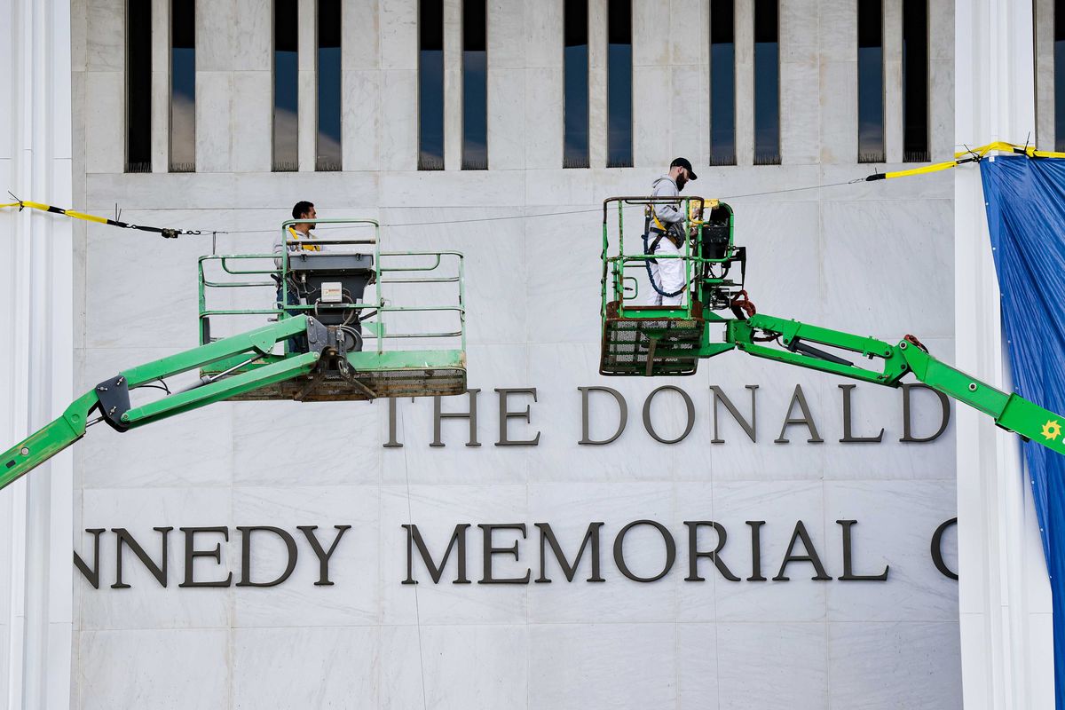 Two green cranes outside the John F. Kennedy Memorial Center for the Performing Arts, which now has 'The Donald J. Trump and...' affixed above the main text.