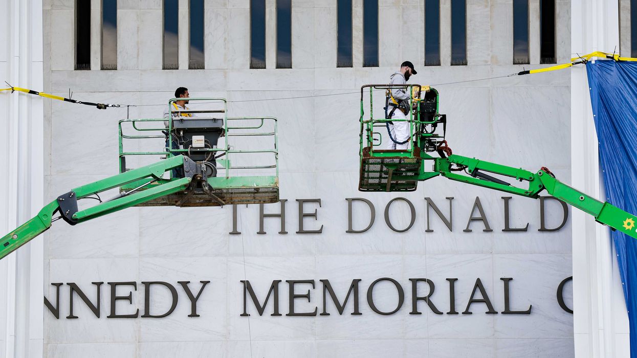 Two green cranes outside the John F. Kennedy Memorial Center for the Performing Arts, which now has 'The Donald J. Trump and...' affixed above the main text.