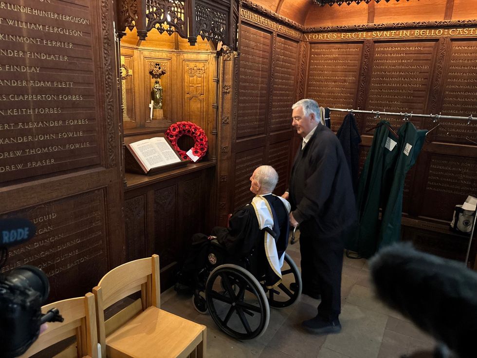 Two men, one in a wheelchair, looking at a poppy wreath