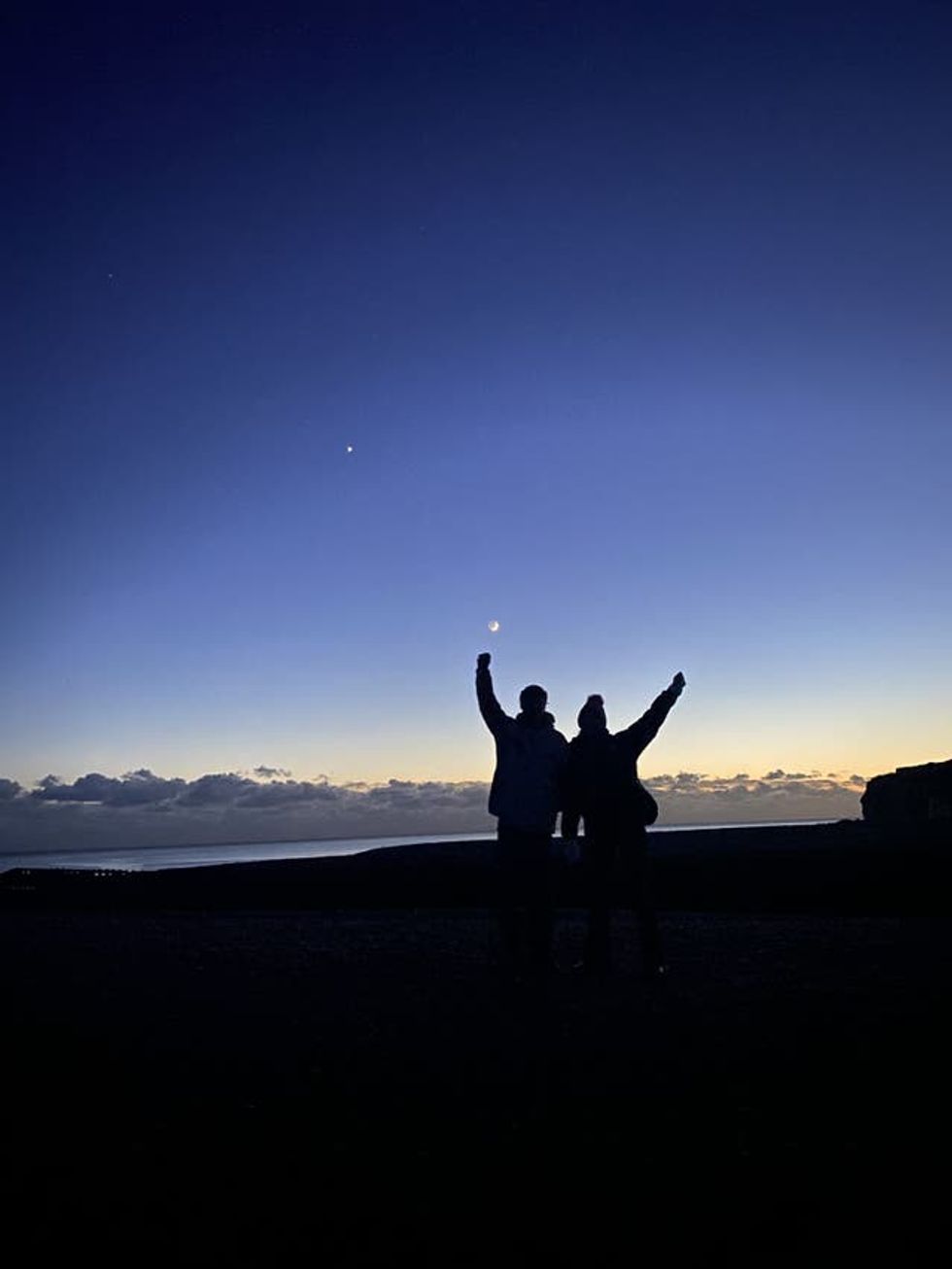 Two people with their arms raised at sunset