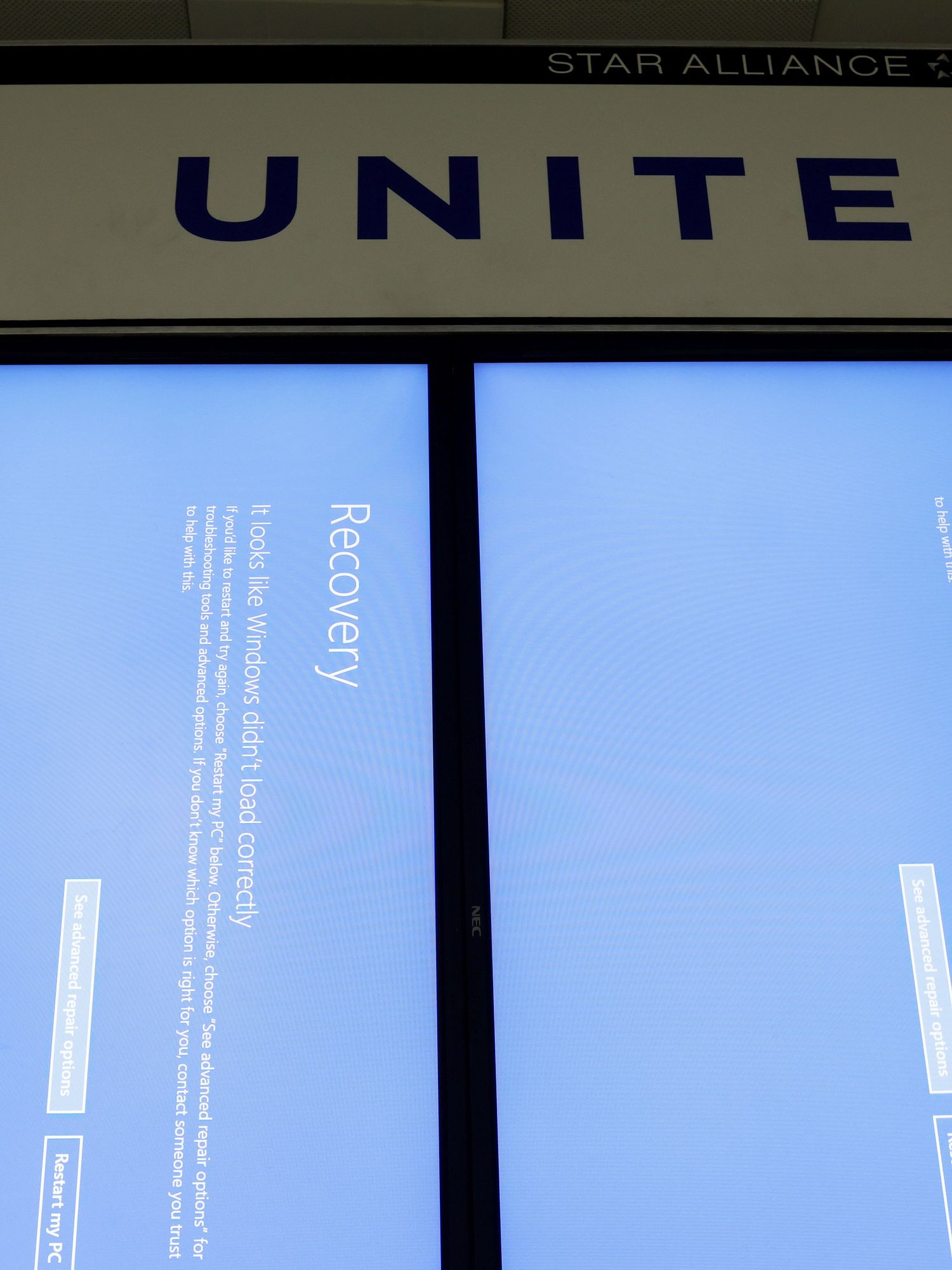 Two portrait computer screens underneath a United sign display a blue 'recovery' message.