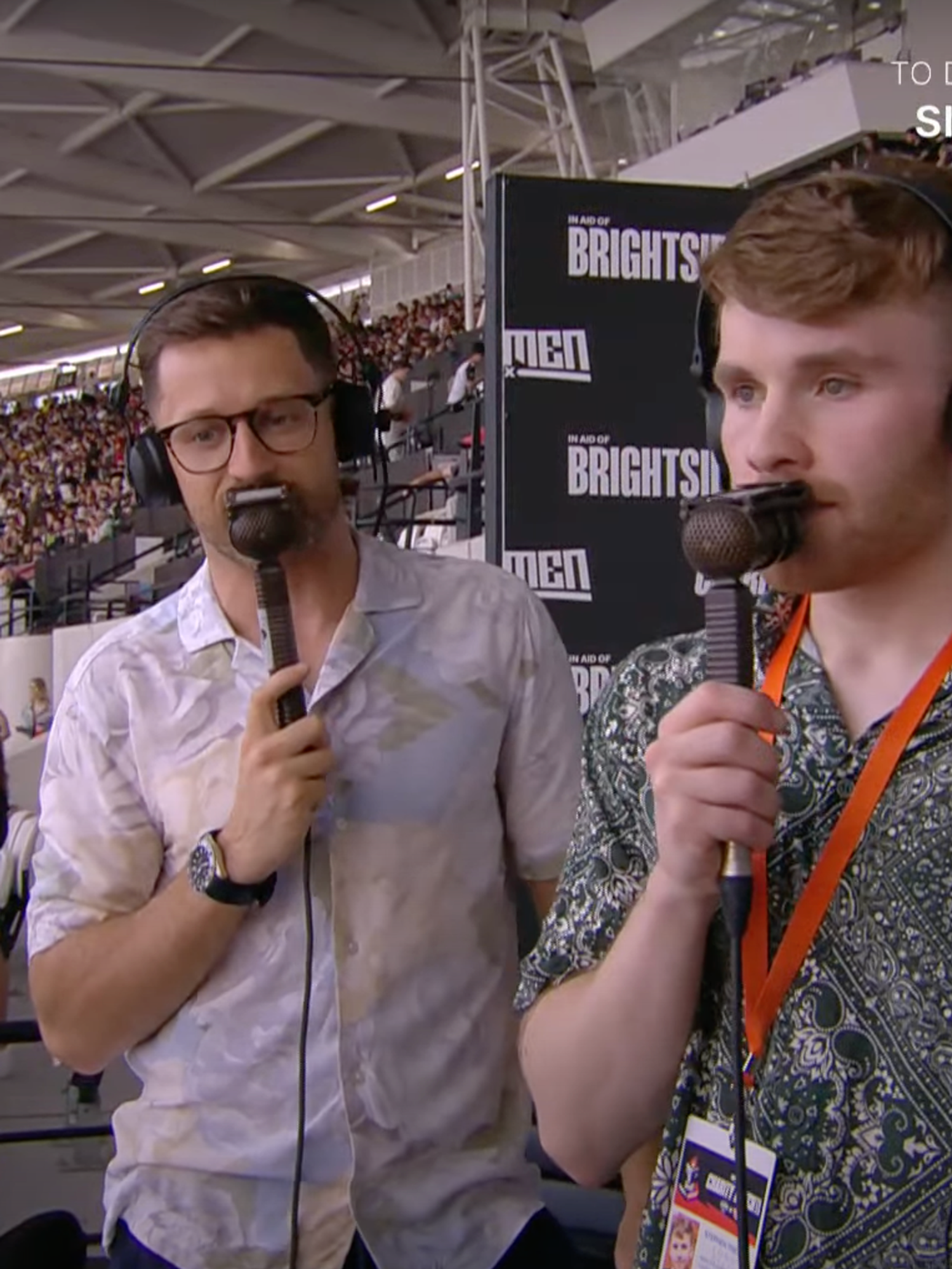 Two white men with commentary microphones in a football stadium.