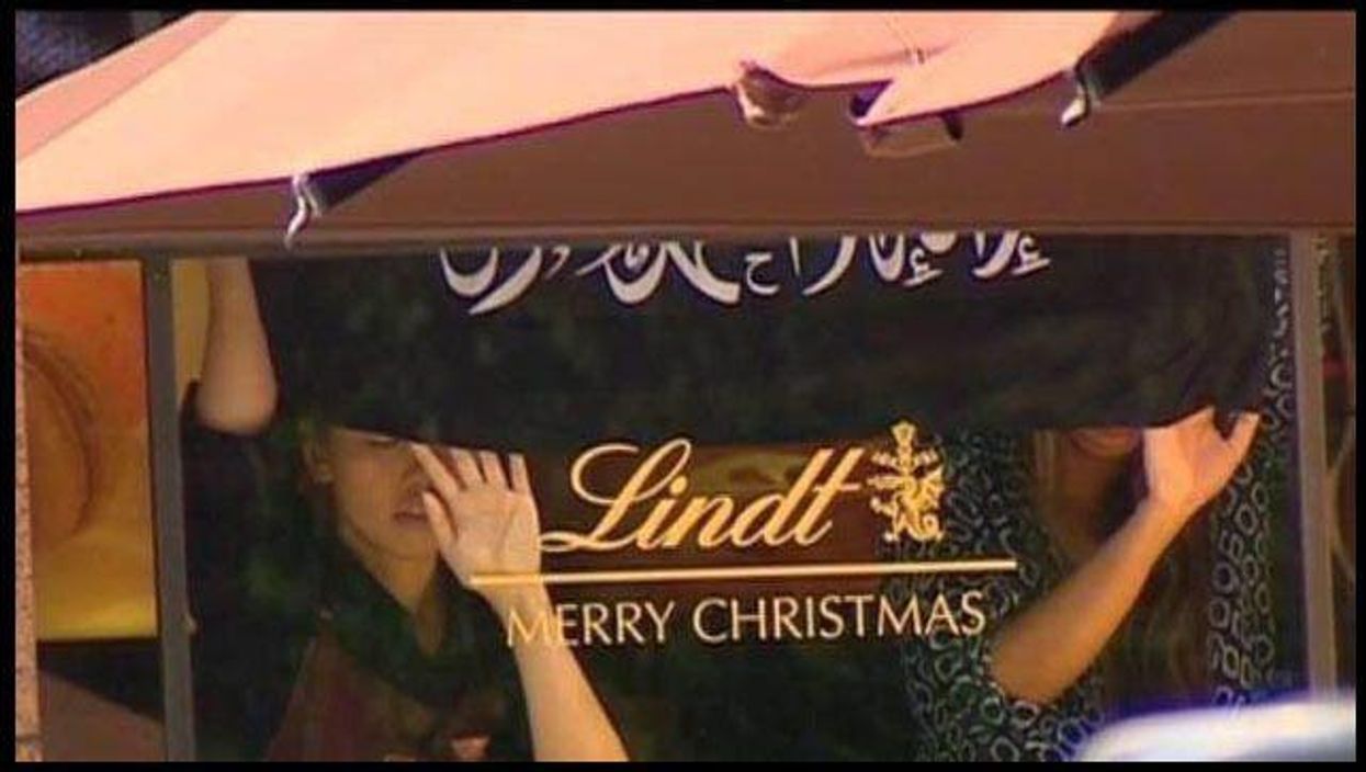 Two women hostages inside the Lindt Cafe holding an islamic flag up against the windo