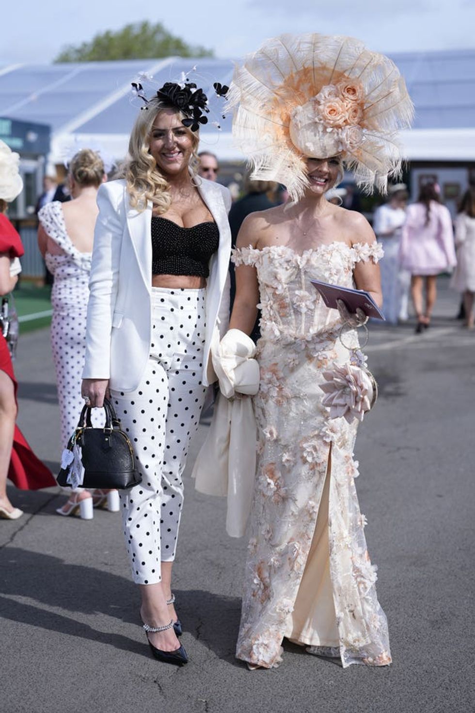 Two women, one in a white and black spotty pants suit and the other is a peach flowered gown with matching hat