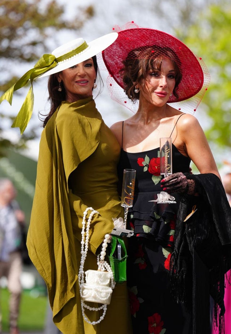 Two women, one in olive green with a white hat and the other in black with a red hat