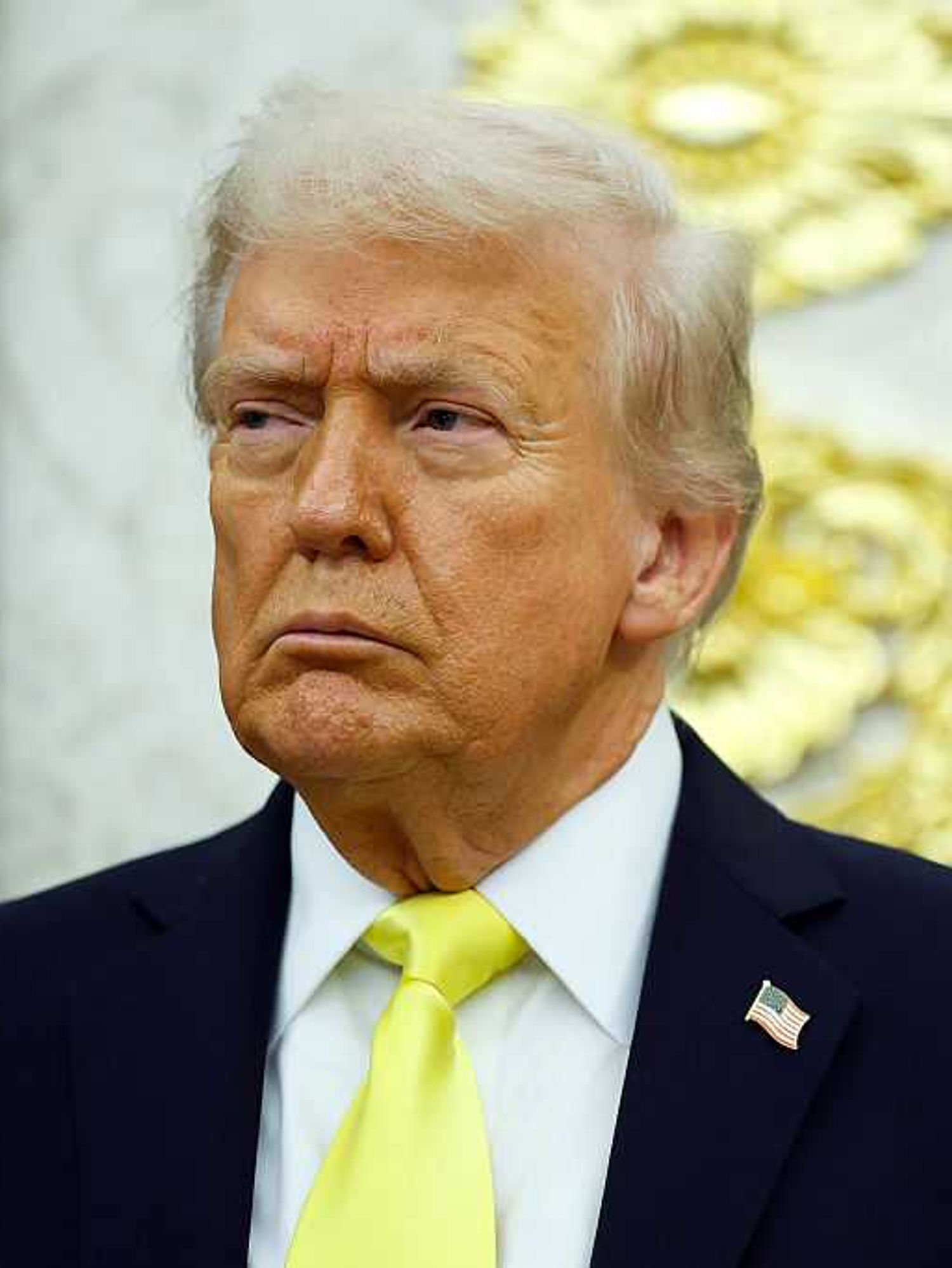 US president Donald Trump, in a black suit with fluorescent yellow tie, frowns as he looks at something off-camera to his right.