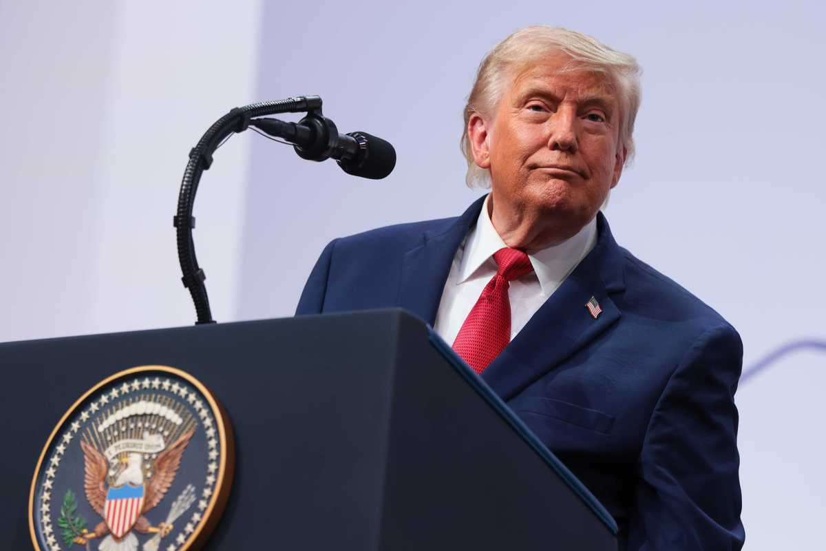 US president Donald Trump in a navy suit and red tie stands behind his presidential lectern on stage.