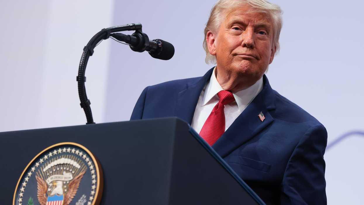 US president Donald Trump in a navy suit and red tie stands behind his presidential lectern on stage.