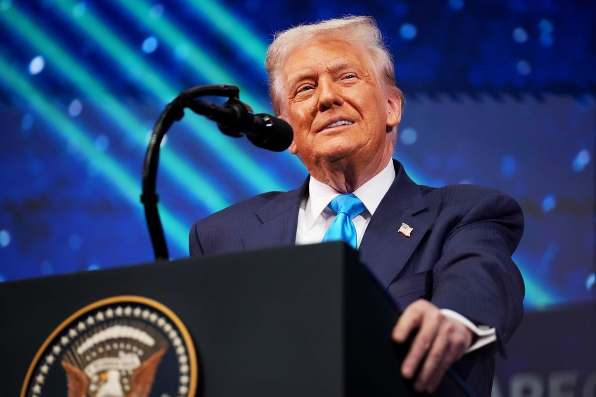US president Donald Trump smiles while standing behind the dark blue presidential lectern.