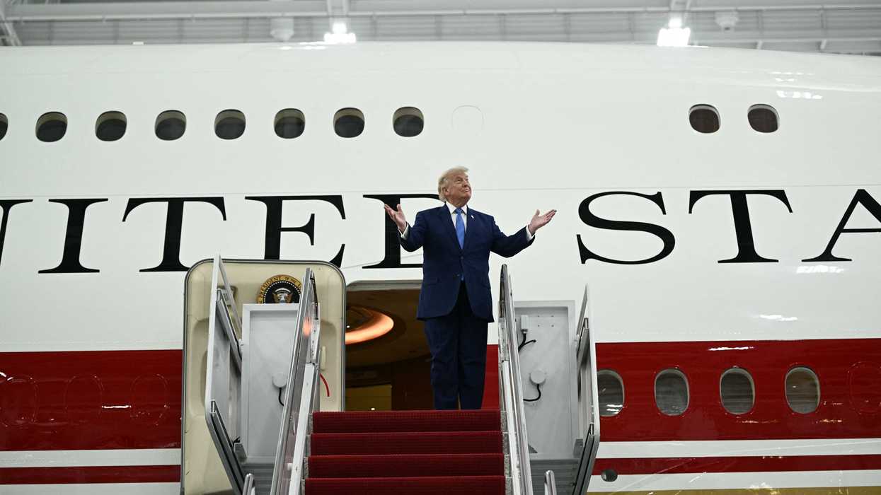 US president Donald Trump standing outside the new Air Force One plane, gesturing with his hands lifted upwards.