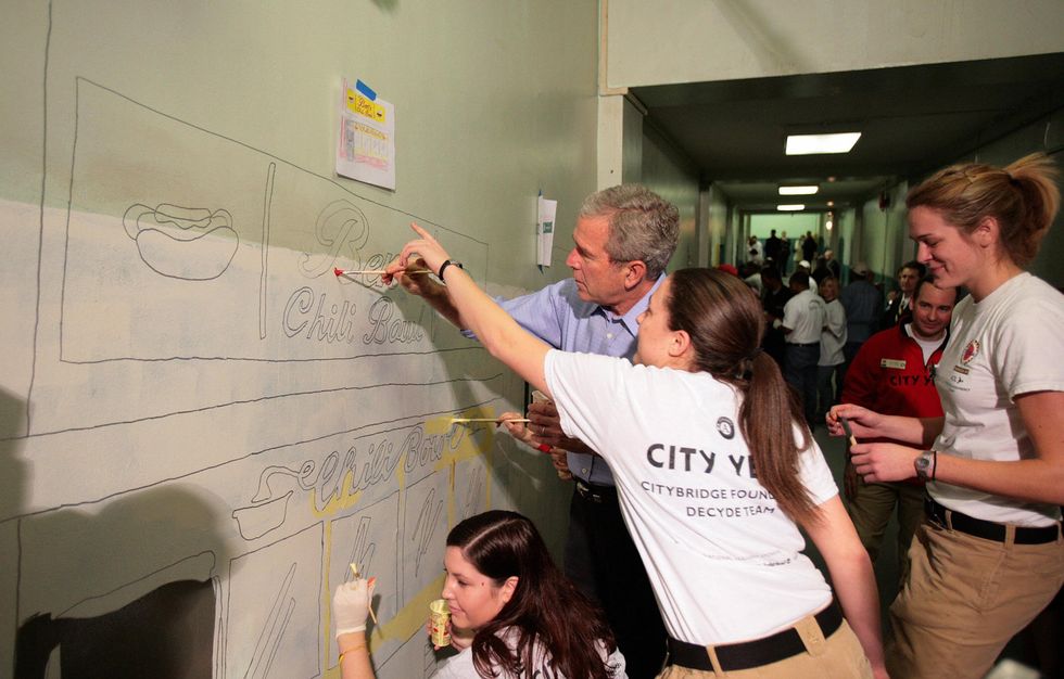 US President George W. Bush (C) is helped by City Year volunteer Morgan Lacey (2nd R) as he paints a mural at Cordozo High School in Washington, DC, 15 January 2007. President Bush made a surprise visit to the school for the Martin Luther King Jr. holiday. Picture: