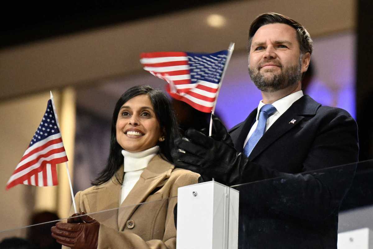 Usha Vance (left) and JD Vance (right) at the Winter Olympics opening ceremony, applauding athletes and holding tiny US flags in their hands.