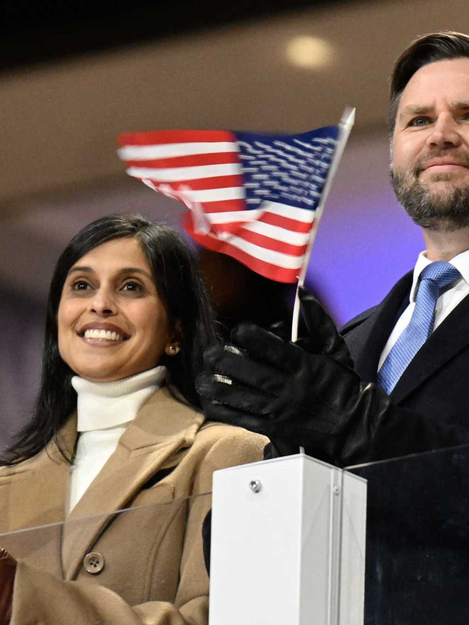 Usha Vance (left) and JD Vance (right) at the Winter Olympics opening ceremony, applauding athletes and holding tiny US flags in their hands.