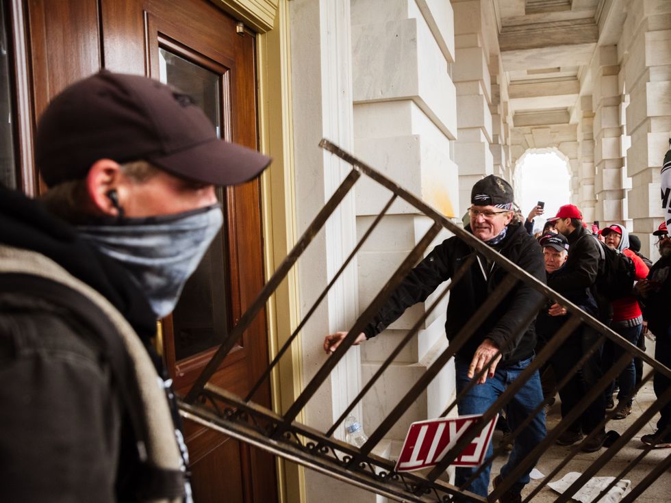 WASHINGTON, DC - JANUARY 06: A member of a pro-Trump mob bashes an entrance of the Capitol Building in an attempt to gain access on January 6, 2021 in Washington, DC. A pro-Trump mob stormed the Capitol, breaking windows and clashing with police officers. Trump supporters gathered in the nation's capital today to protest the ratification of President-elect Joe Biden's Electoral College victory over President Trump in the 2020 election. (Photo by Jon Cherry/Getty Images)