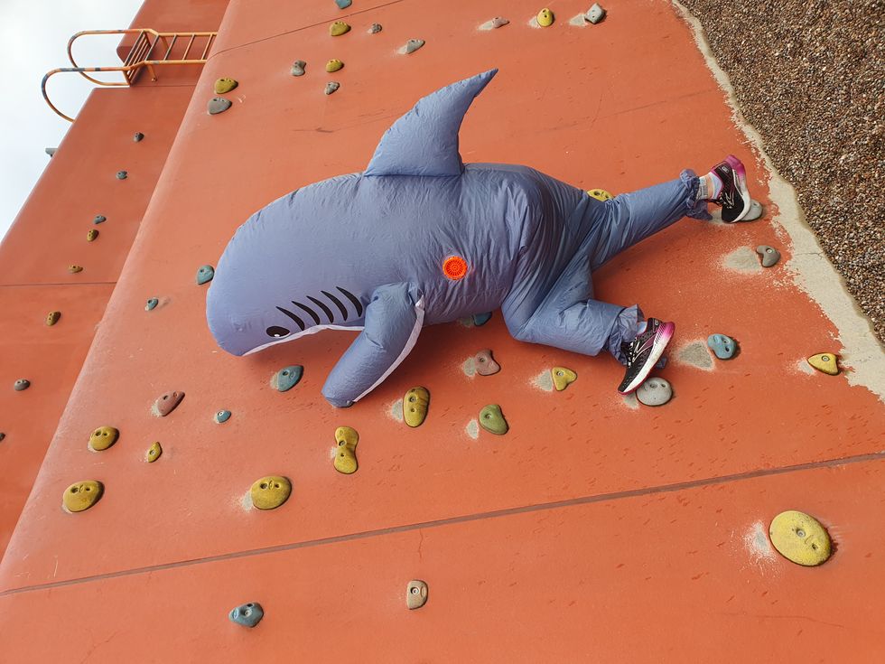 Woman climbing wall in inflatable shark costume