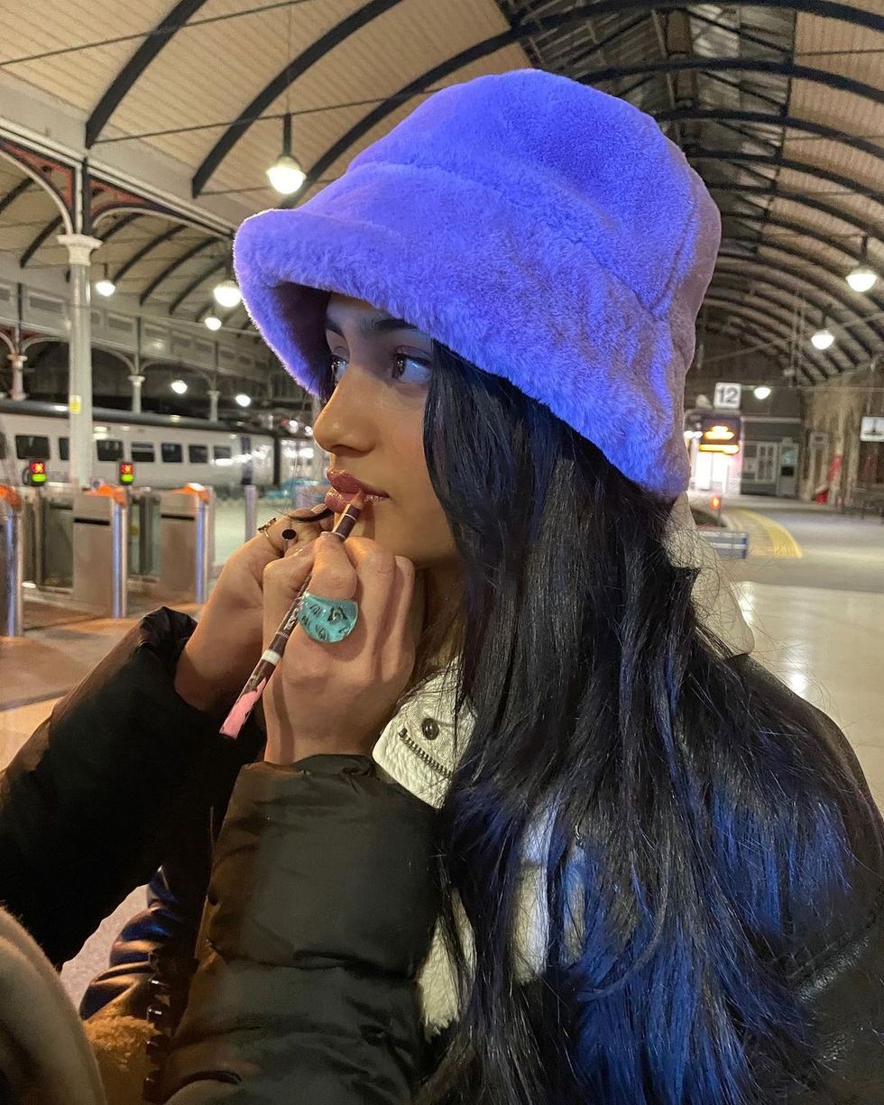 Woman wearing a hat and someone putting lipstick on her