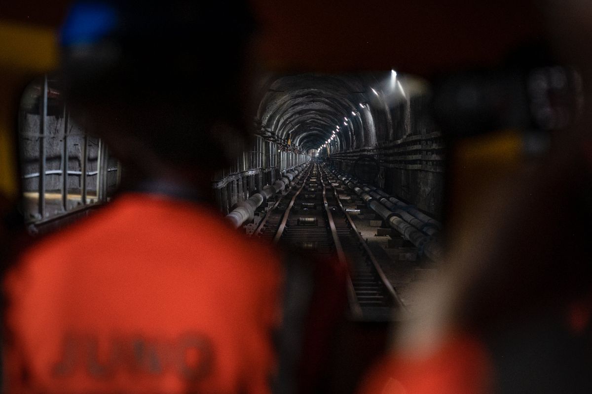 Workers wearing high-vis vests look down a train tunnel