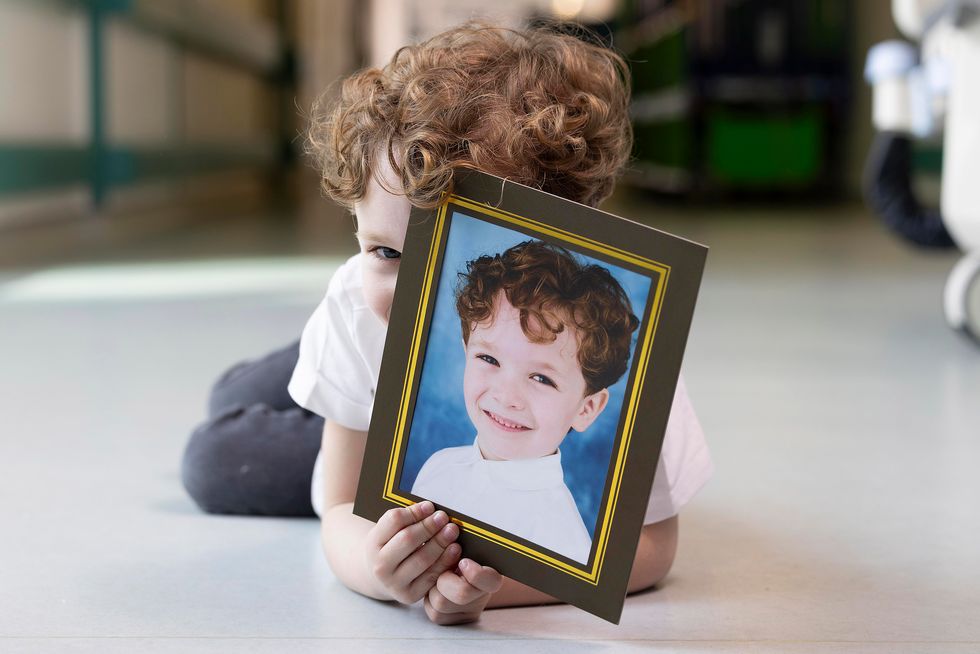 Young boy holding a school day-style portrait of himself in front of his face