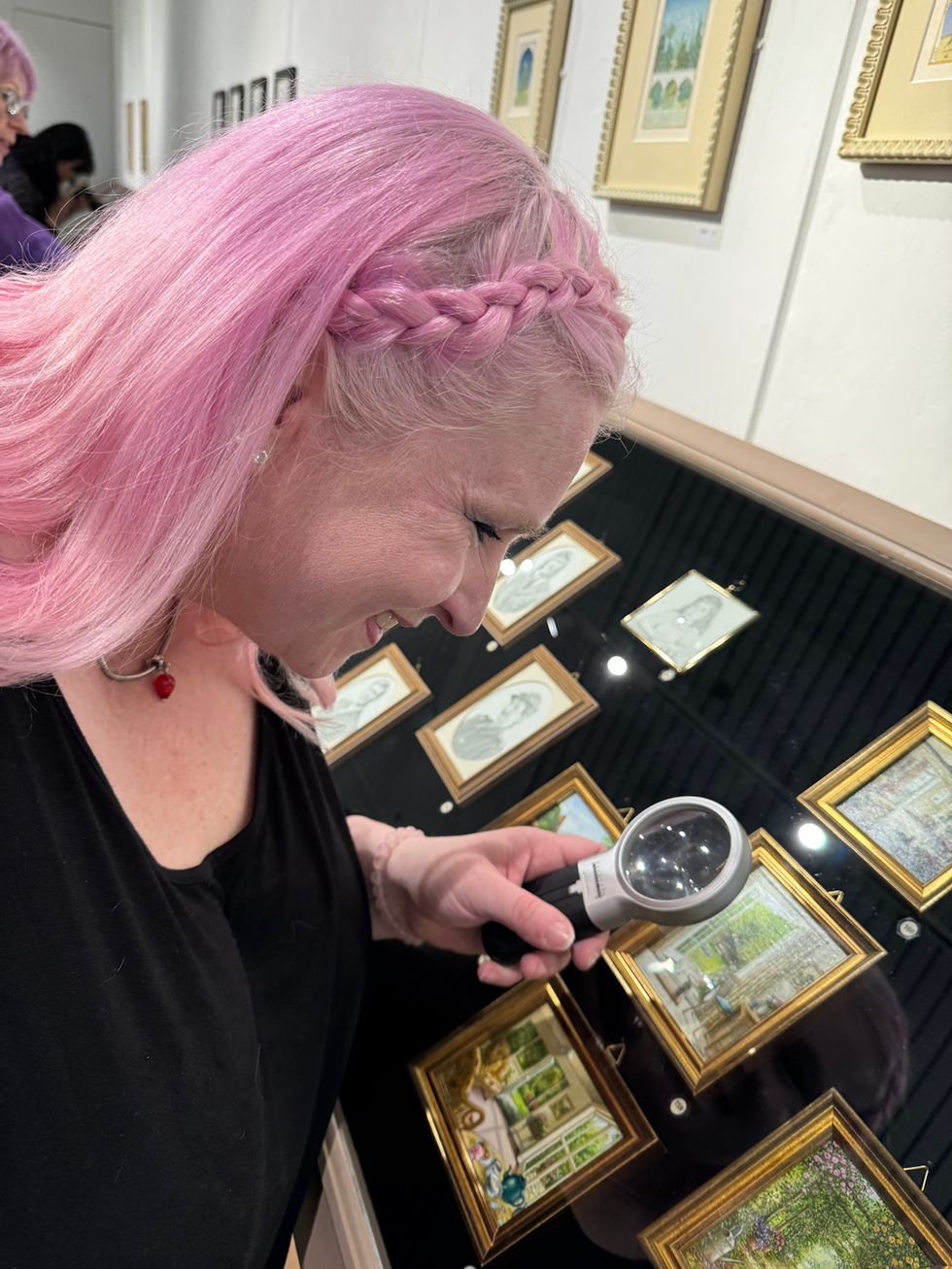 Yvonne Jack using a magnifying glass to look at a series of miniature artworks