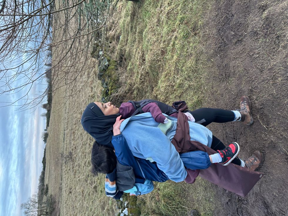 Zahrah Mahmood walking outdoors with a baby on her chest and toddler on her back