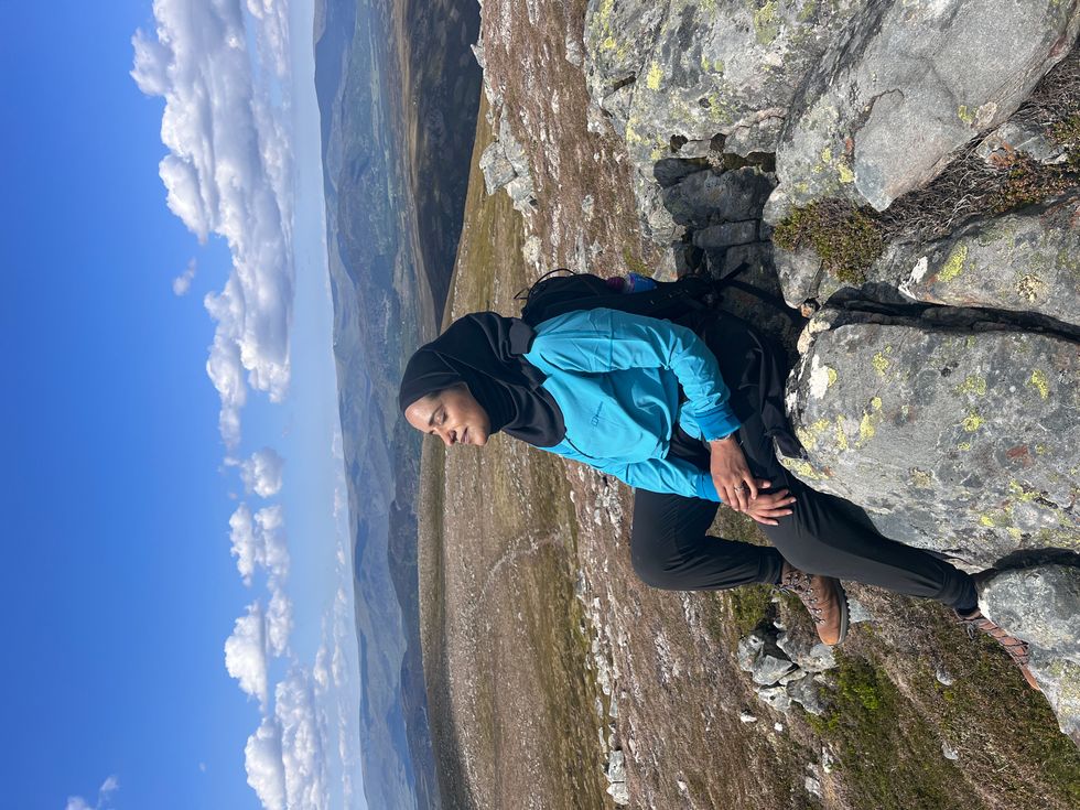 Zahrah Mahmood with her eyes closed and facing the sun, on a mountain with blue skies above