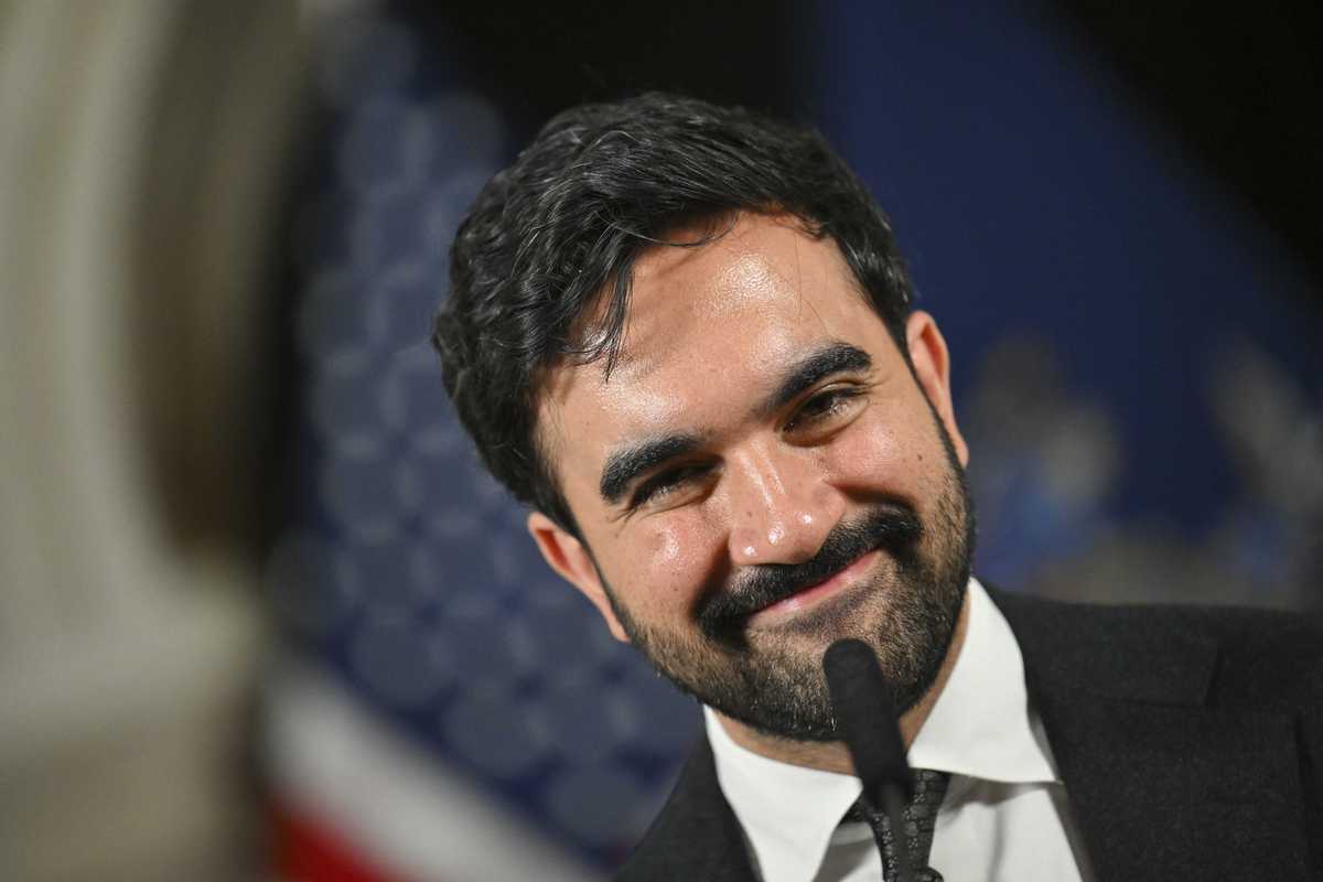 Zohran Mamdani smiles in front of a microphone.